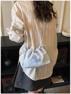 Detail of light blue bucket bag featuring a purple plush pony patch and yellow stitching