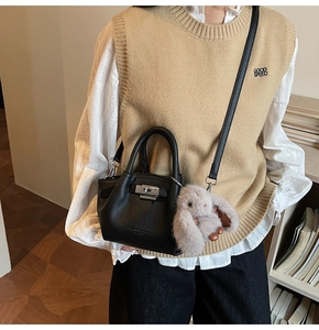 Detail of black lychee grain leather bucket bag with silver twist lock and plush rabbit charm