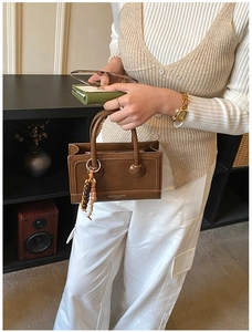 Detail of a brown vintage square handbag with a bohemian beaded charm and top handle
