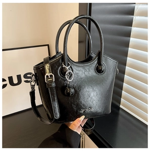 Detail view of glossy black trapezoid bucket bag with metal ball charm and JFYDS logo