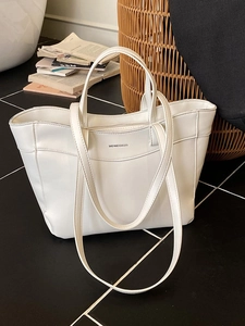 Minimalist white leather tote bag with handle and shoulder strap in a cozy home setting