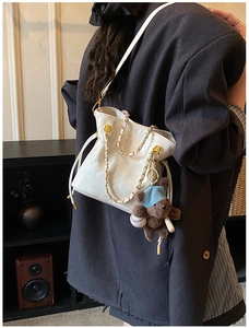 Detail of white quilted bucket bag featuring a gold chain and cute brown bear charm