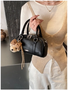 Detail of a black leather Boston bag featuring a plush bear charm and metallic hardware