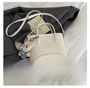 Detail of cream tote bag with round handle, teddy bear charm and brand logo lettering