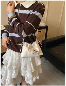 Detail of white drawstring bucket bag with horse embroidery on striped knit sweater