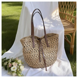 Detail of woven straw tote bag with brown leather handles and drawstring closure on fabric
