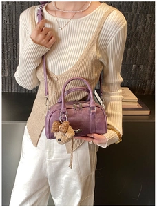 Close-up of a purple Boston bag with a teddy bear charm worn by a model in a knit sweater