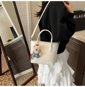 Close-up of cream white bucket bag with detachable strap and cute teddy bear pendant