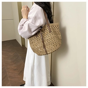 Detail showing hollow woven texture and brown leather strap of the large straw tote bag