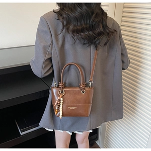 Detail of a dark brown glossy mini tote bag with beaded charm and gold text on a grey blazer