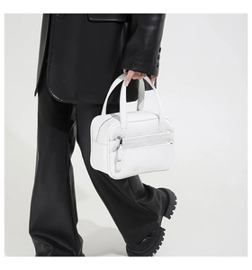 Detail of a white pebbled leather briefcase held by a model in a black leather suit