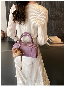 Close-up of a purple faux leather Boston bag with dog plush charm on a model