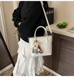 Detail of a white bucket bag with detachable strap and a blue teddy bear charm