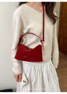 Dettaglio borsa a spalla in pelle rossa con fibbia dorata su modella in abito bianco