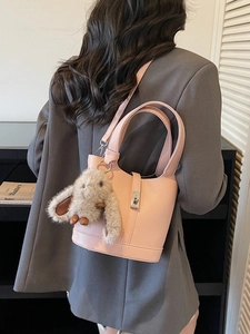 Pink pebbled leather bucket bag with silver buckle and plush rabbit charm on a grey blazer