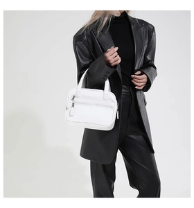 Close-up of a white lychee grain leather Boston bag held by a model in a black blazer
