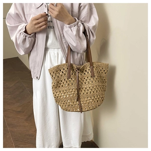 Close-up of hollow woven tote bag featuring dark brown leather handles and drawstring closure