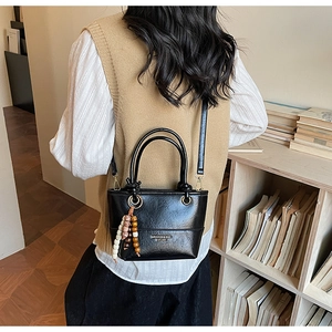 Detail of a chic black bucket bag with gold hardware and colorful beaded keychain