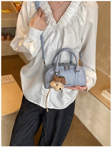 Detail of light blue Boston handbag with plush puppy charm on a white ruffled shirt