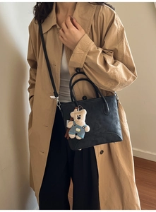 Detail of black leather bucket bag with a cute teddy bear charm and logo embossing