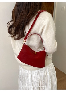Dettaglio della borsa in pelle rossa con chiusura dorata su maglione bianco