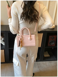Detail of light pink rectangular bag with wooden bead charm and long shoulder strap