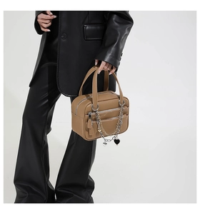 Close-up of brown leather Boston bag featuring multiple zippers and a heart pendant