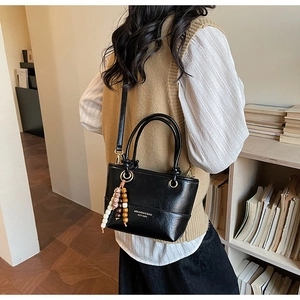 Detail of black leather tote bag with elegant wooden bead charm and gold logo lettering