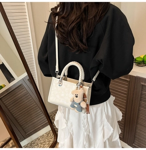 Detail of white square handbag with woven handle, teddy bear charm, and leather strap