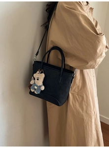 Black matte leather bucket bag with a cute bear charm accessory on a beige trench coat