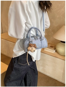 Detail of light blue cylinder bag with silver zipper and cute plush dog charm