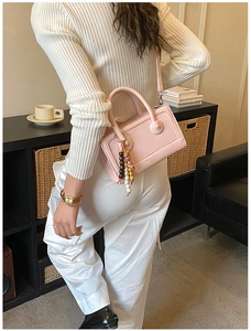 Detail of a pink vintage crossbody bag with beaded charm worn by a model in a cozy room