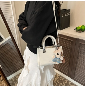 On-body view of cream white crossbody bag with braided handle and bear charm pendant