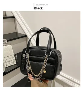 Detail of black textured leather Boston bag featuring layered gold and silver chain charms