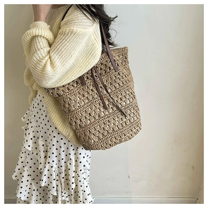 Detail of woven mesh tote bag featuring dark brown leather straps and drawstring accents