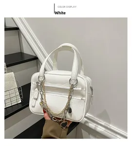 Detail of white lychee leather handbag with colorful metal chains and heart pendant