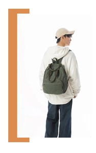 Detail of dark green canvas backpack featuring rounded design and front zipper pocket