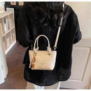 Detail of cream bucket bag with unique knot handles and elegant wooden bead charm