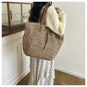 Close-up of a large woven tote bag with brown leather straps and detailed crochet texture