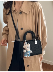 Detail of black faux leather crossbody bag with woven handle and plush bear charm