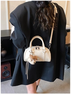 Chic cream Boston handbag with plush bear charm and adjustable shoulder strap worn with blazer