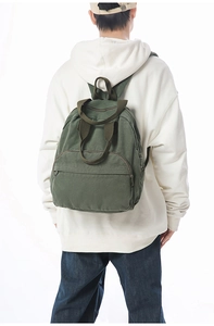 Rear view of a model wearing the army green canvas backpack on a white background