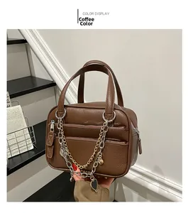 Detail view of coffee-colored Boston bag with dual zippers and heart chain accent