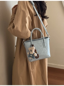 Detail of matte leather bucket bag with brand embossing and cute teddy bear charm