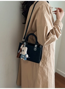 Detail of minimalist black tote bag featuring woven handle and cute plush bear charm