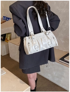 Side view of white patent leather shoulder bag with silver buckles and ruched details