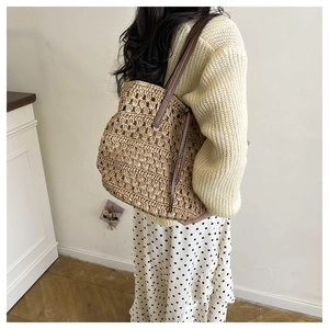 Detail of hollow-out beige woven tote bag with brown leather handles and side drawstrings