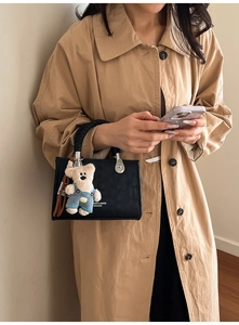 Detail of black leather tote with woven handle and cute bear charm on a trench coat