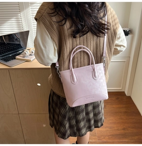 Close-up of a pale pink matte leather tote bag with brand embossing and slim shoulder strap