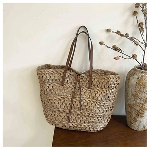 Detailed view of hand-woven hollow tote bag with leather handles on a wooden table